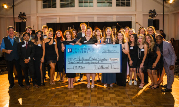 A large group of people pose indoors at a fundraising gala, holding an oversized $360,000 check made out to Northwood University Student Scholarships, dated 9/19/2025—supporting the future of automotive education.