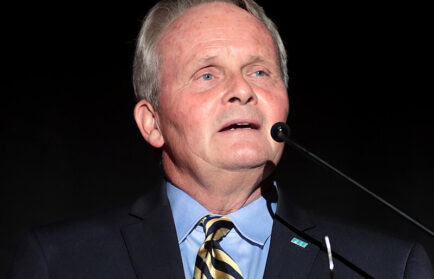 A man in a suit and striped tie speaks at a podium with a microphone in front of a dark background at the Freedom Seminar.