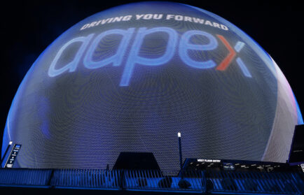 At night, a large spherical display lights up with "DRIVING YOU FORWARD," "aapex," and a nod to AAPEX 2025 in bold blue and red letters.