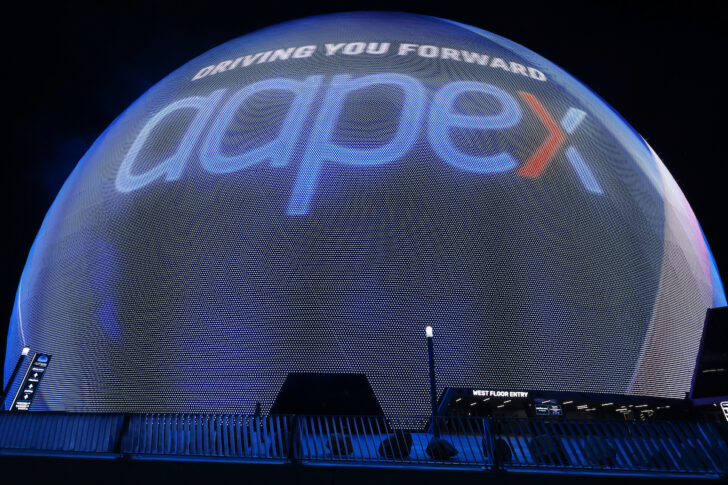 At night, a large spherical display lights up with "DRIVING YOU FORWARD," "aapex," and a nod to AAPEX 2025 in bold blue and red letters.