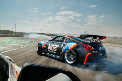 A black and blue sports car with NOS Energy Drink branding drifts around a racetrack, producing smoke from the tires—a thrilling display of motorsports at its finest.