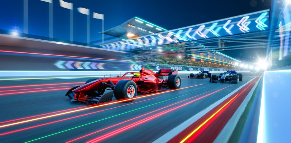 A red Formula 1 race car, exemplifying elite Motorsports Management, leads on a brightly lit racetrack at night, followed by other cars, with motion blur emphasizing high speed.