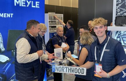 A group of people stand and interact at a trade show booth featuring a "NORTHWOOD" sign, brochures, and a QR code, with MEYLE branding visible in the background.
