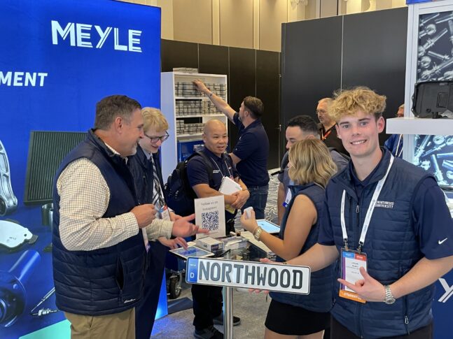 A group of people stand and interact at a trade show booth featuring a "NORTHWOOD" sign, brochures, and a QR code, with MEYLE branding visible in the background.