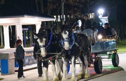 Two decorated horses pull a lit-up wagon with people on board at night, near a Northwestern University sign and a small pavilion—capturing the spirit of Winter Wonderland enhancements on Dec. 9.