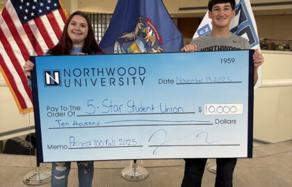 Two students hold a large check for $10,000 from Northwood University made out to “5-Star Student Union,” dated November 19, 2025, with American and Michigan flags behind them.