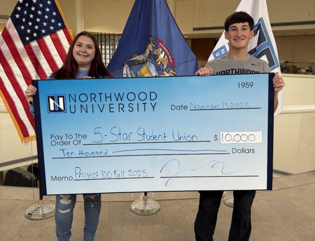 Two students hold a large check for $10,000 from Northwood University made out to “5-Star Student Union,” dated November 19, 2025, with American and Michigan flags behind them.