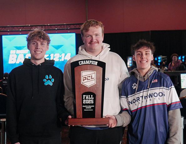 Three young men stand indoors, smiling and holding a large "Champion PCL Fall 2023" trophy. The background displays gaming monitors and a blue screen with text.