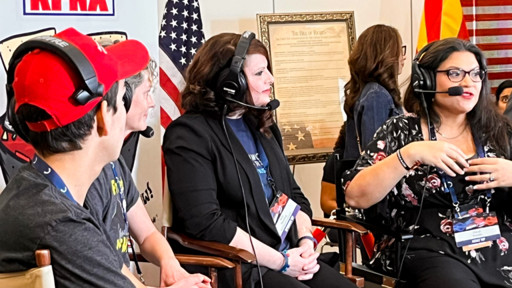 Four people wearing headsets sit and talk in a studio, with American flags and the Declaration of Independence displayed in the background, representing Turning Point USA Northwood.
