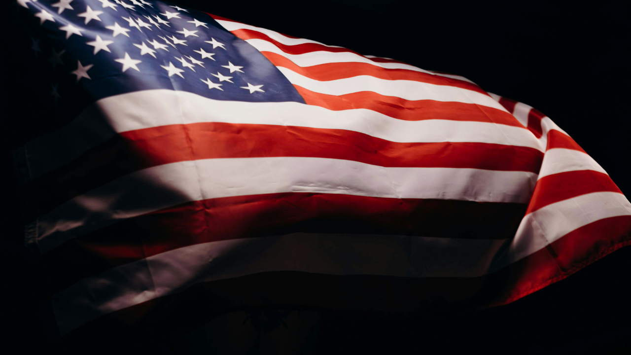 A close-up of an American flag with visible stars and stripes, waving against a dark background, captures the spirit of Turning Point USA Northwood.