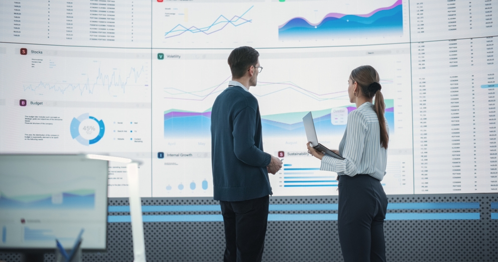 A man and woman reviewing accounting data on a large screen.