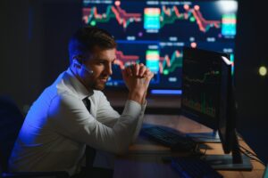 A man wearing a headset sits at a desk, analyzing accounting data and financial charts on his monitors in a dark office with large screens in the background.