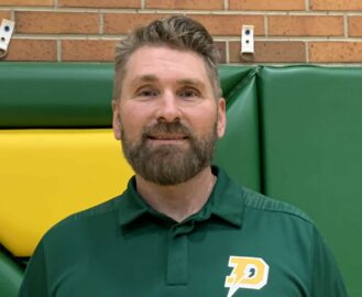 A man with short hair and a beard, wearing a green collared shirt with a yellow "P" logo, stands in front of a gym wall with green and yellow padding, representing the spirit of Esports management.