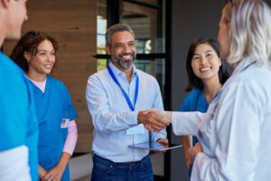 A group of healthcare professionals and administrators stand together, with one man in business attire shaking hands with a doctor.