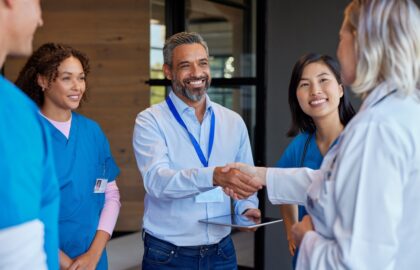 A group of healthcare professionals and administrators stand together, with one man in business attire shaking hands with a doctor.