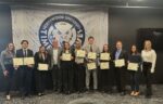 A group of people in business attire stand in front of a Northwood University banner, with several holding certificates and posing for a group photo.