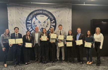 A group of people in business attire stand in front of a Northwood University banner, with several holding certificates and posing for a group photo.