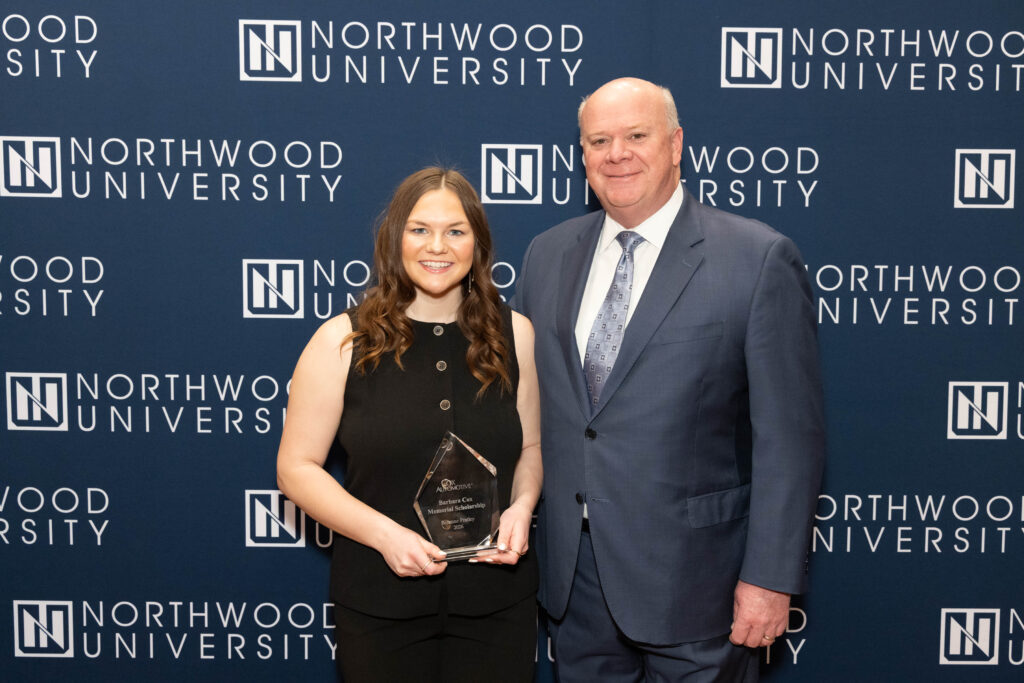 A woman holding an award stands next to a man in a suit, both posing in front of a Northwood University backdrop—celebrating the achievements of Future Professionals and emerging Automotive Leaders.