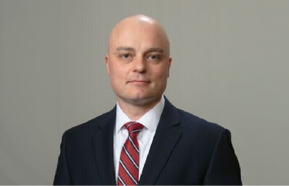 A man in a dark suit, white shirt, and red striped tie poses against a plain, light-colored background, exuding confidence and Leadership Insights.