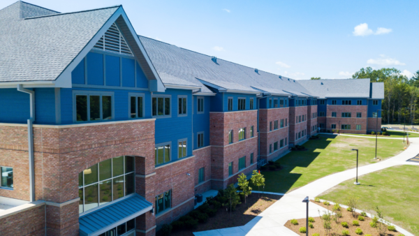 A modern, three-story building with blue siding and a brick exterior, surrounded by grass and walkways, welcomes visitors on a sunny day—an ideal setting for Undergraduate Admissions.