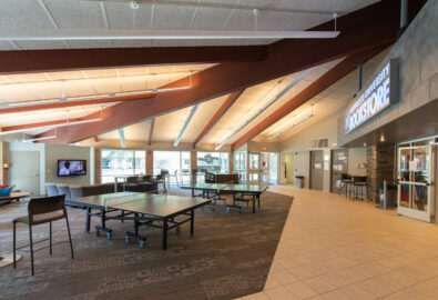 A spacious student center with ping pong tables, chairs, large windows, and a campus bookstore under a sloped ceiling with exposed beams—part of Northwood's Project 100 initiative.