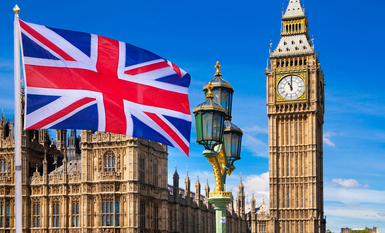Union Jack flag flying near a decorative lamp post, with the clock tower known as Big Ben and the Houses of Parliament under a clear blue sky in London—a perfect spot to explore with family or friends.