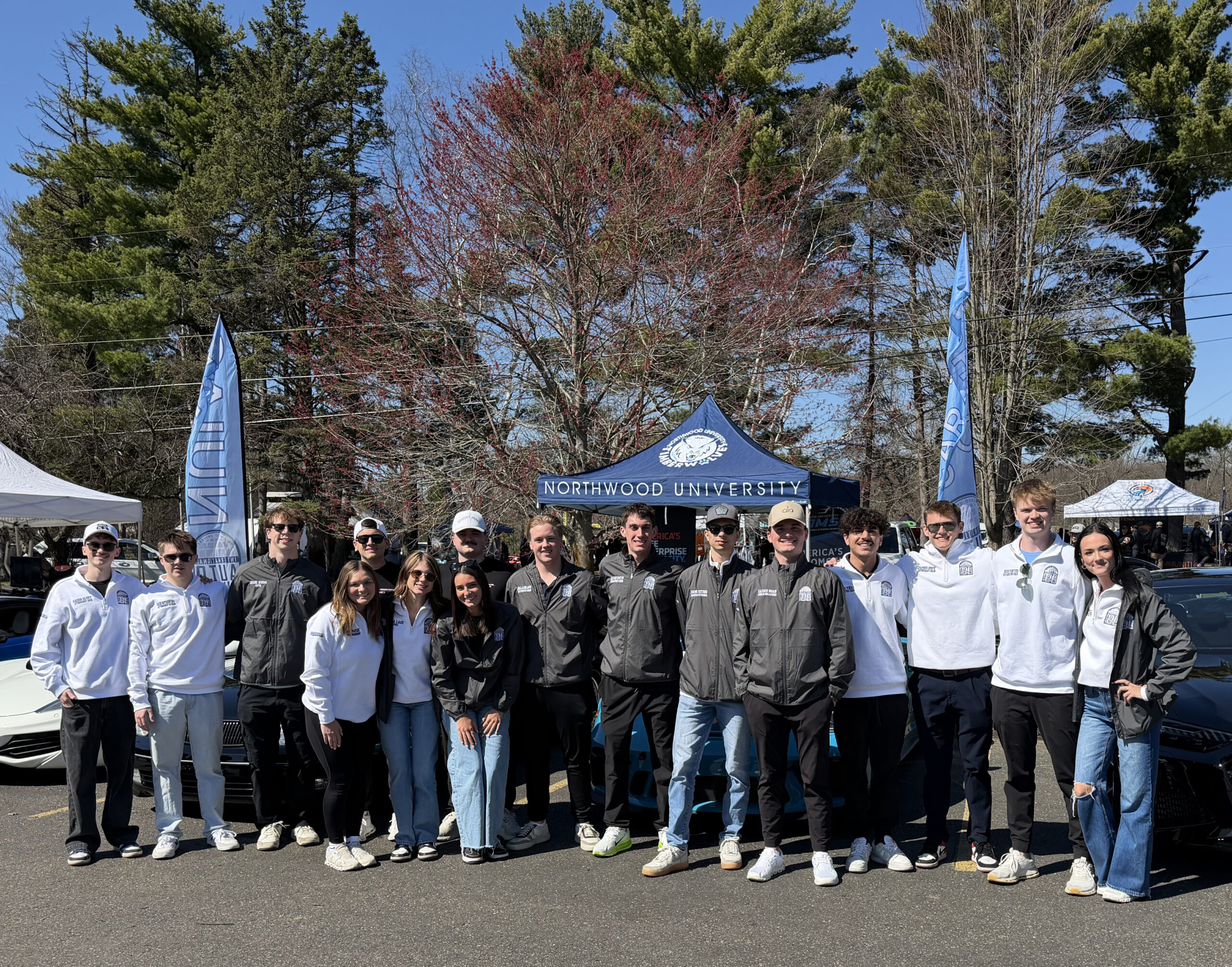 A group of people stand in front of a Northwood University canopy tent outdoors, with trees in the background on a sunny day.