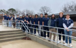 A group of students wearing matching navy blue t-shirts stands in a line along a ramp outdoors on a cloudy day, representing Northwood University’s commitment to Cybersecurity excellence.