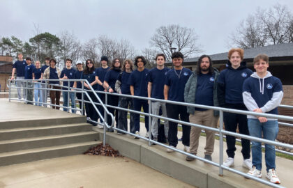 A group of students wearing matching navy blue t-shirts stands in a line along a ramp outdoors on a cloudy day, representing Northwood University’s commitment to Cybersecurity excellence.