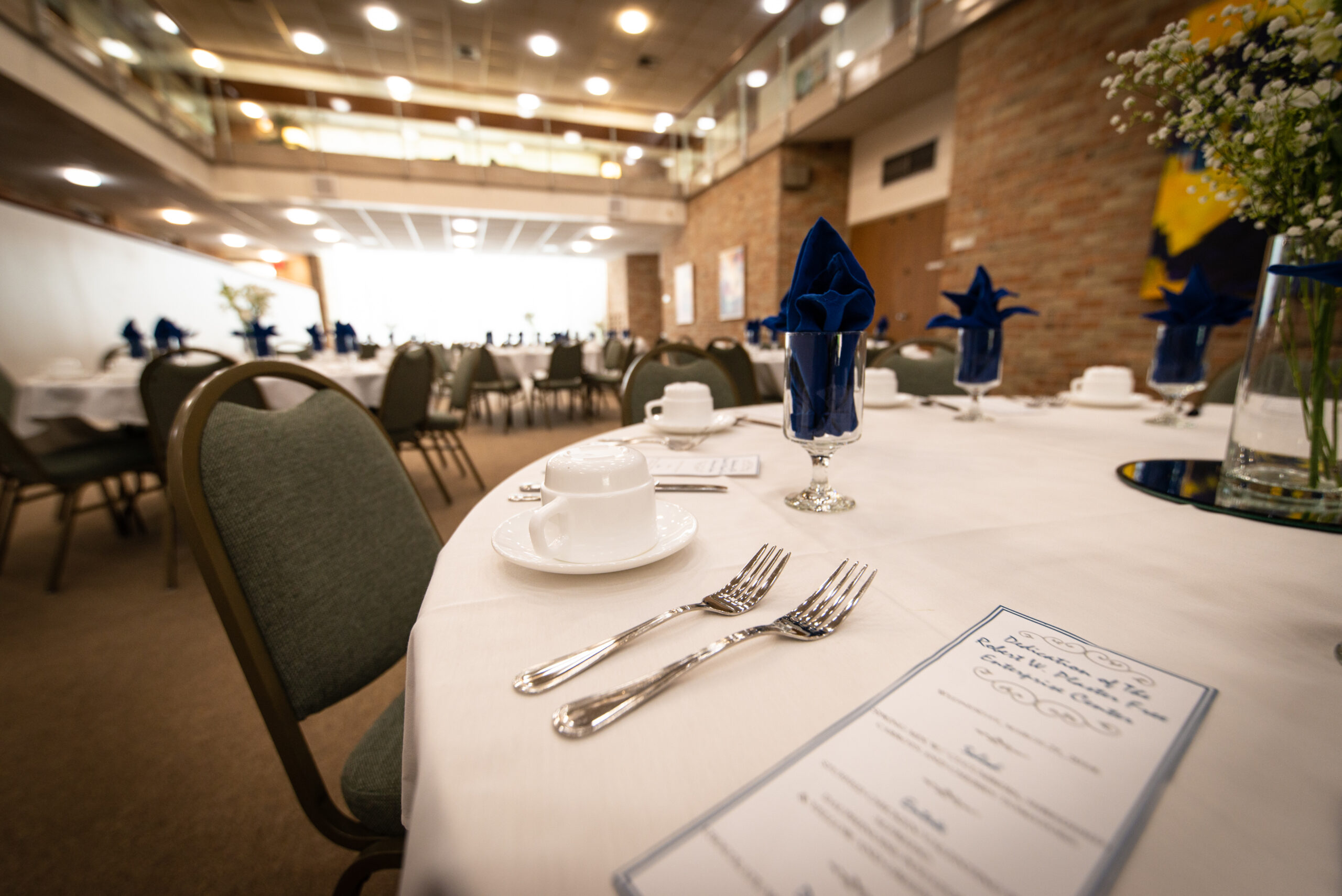 A round table set for a formal event with white tablecloth, silverware, menu, glass with blue napkin, and chairs in a spacious venue—perfect for networking or discussing top sports marketing jobs.