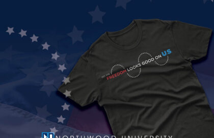 Black t-shirt with the text "Freedom looks good on us" displayed on a background featuring the Northwood University logo, stars, and part of the American flag—a Limited-Edition Apparel piece celebrating how Freedom Lights the Future.