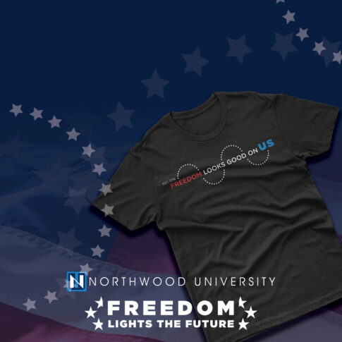 Black t-shirt with the text "Freedom looks good on us" displayed on a background featuring the Northwood University logo, stars, and part of the American flag—a Limited-Edition Apparel piece celebrating how Freedom Lights the Future.