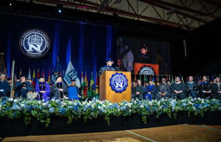A speaker in academic regalia addresses an audience from a podium at a university commencement celebration, with faculty and officials seated on stage, highlighting the balance of freedom and responsibility that accompanies graduation.