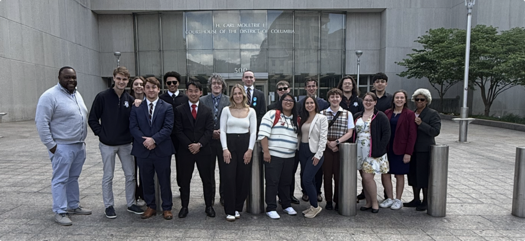 A group of people poses for a photo outside the H. Carl Moultrie I Courthouse of the District of Columbia.