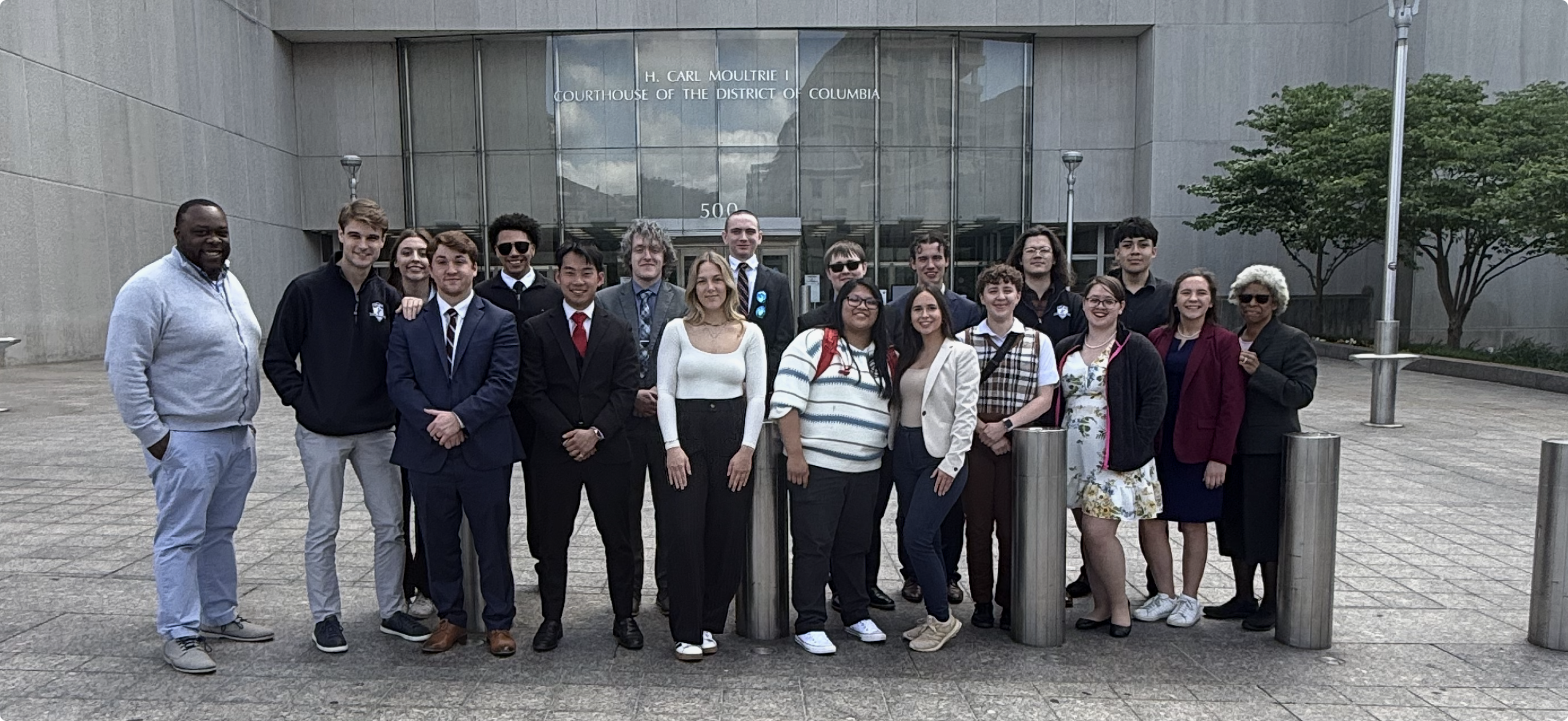 A group of people poses for a photo outside the H. Carl Moultrie I Courthouse of the District of Columbia.