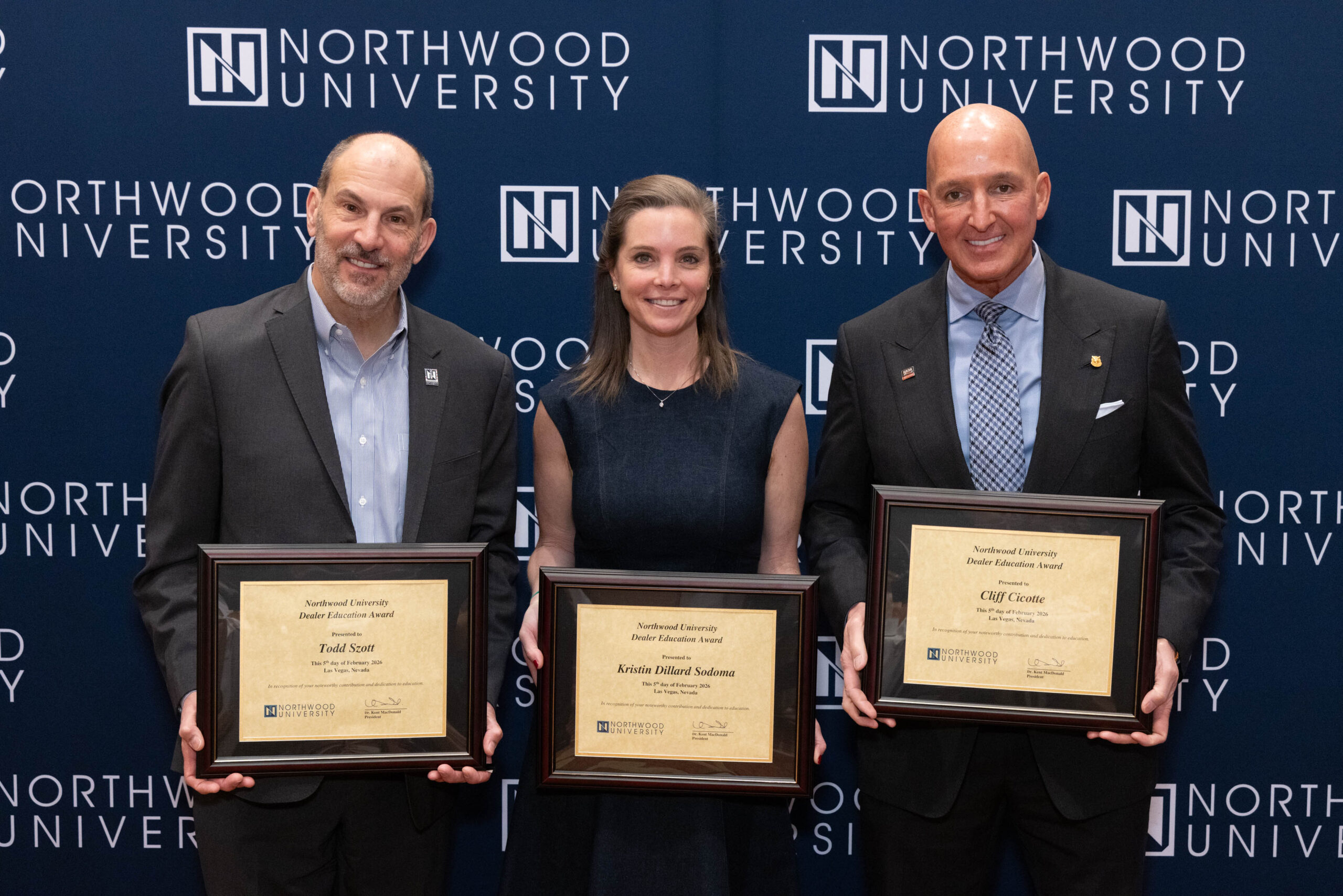 Three people stand in front of a Northwood University backdrop, each holding a framed award certificate, celebrating excellence in university automotive achievements.