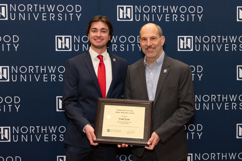 Two men stand in front of a Northwood University automotive backdrop, with one holding a framed certificate that reads "Todd Scott.