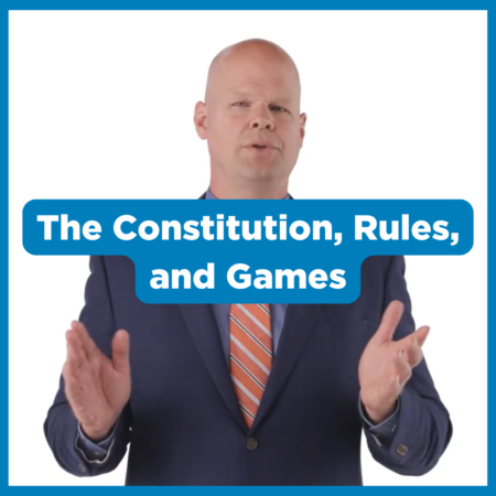 A man in a blue suit and striped tie gestures with his hands. Overlaid text reads, โThe Constitution, Rules, and Games,โ highlighting the importance of the US Constitution and its role in shaping our national holiday, Constitution Day.