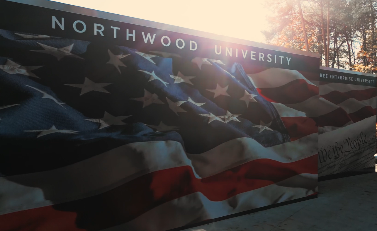 A large American flag mural is displayed on a wall at Northwood University with sunlight filtering through trees in the background, creating a patriotic scene perfect for celebrating Constitution Day.