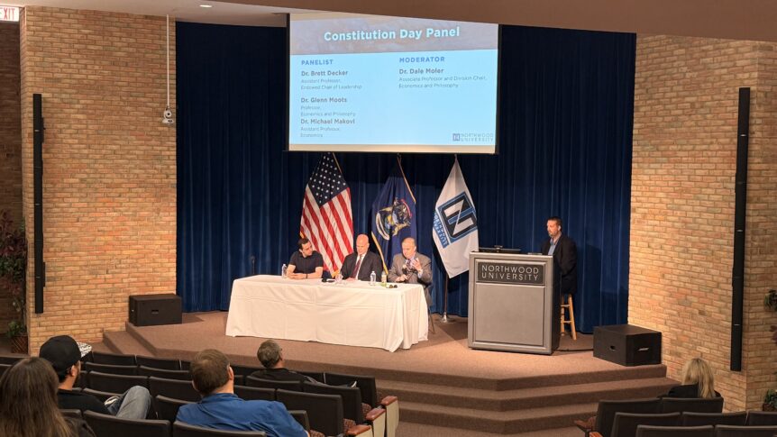 Four panelists sit at a table on stage with U.S. and Michigan flags, as a moderator stands at a podium during Northwood University’s Constitution Day Panel, engaging in thoughtful discussion about America’s Governing Framework.
