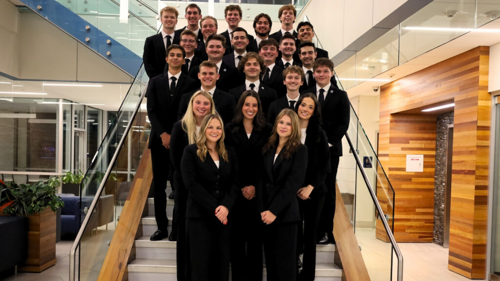 A group of people in black suits stands together on a staircase inside a modern building, posing for a formal group photo.