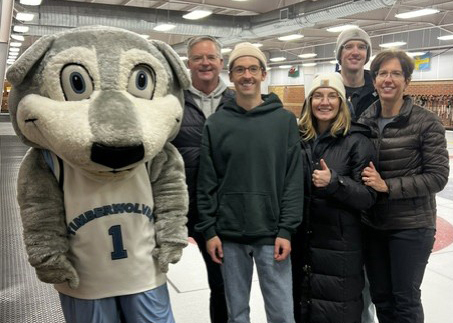 A group of five people poses with a Timberwolves mascot on an indoor curling rink during a fundraiser event.