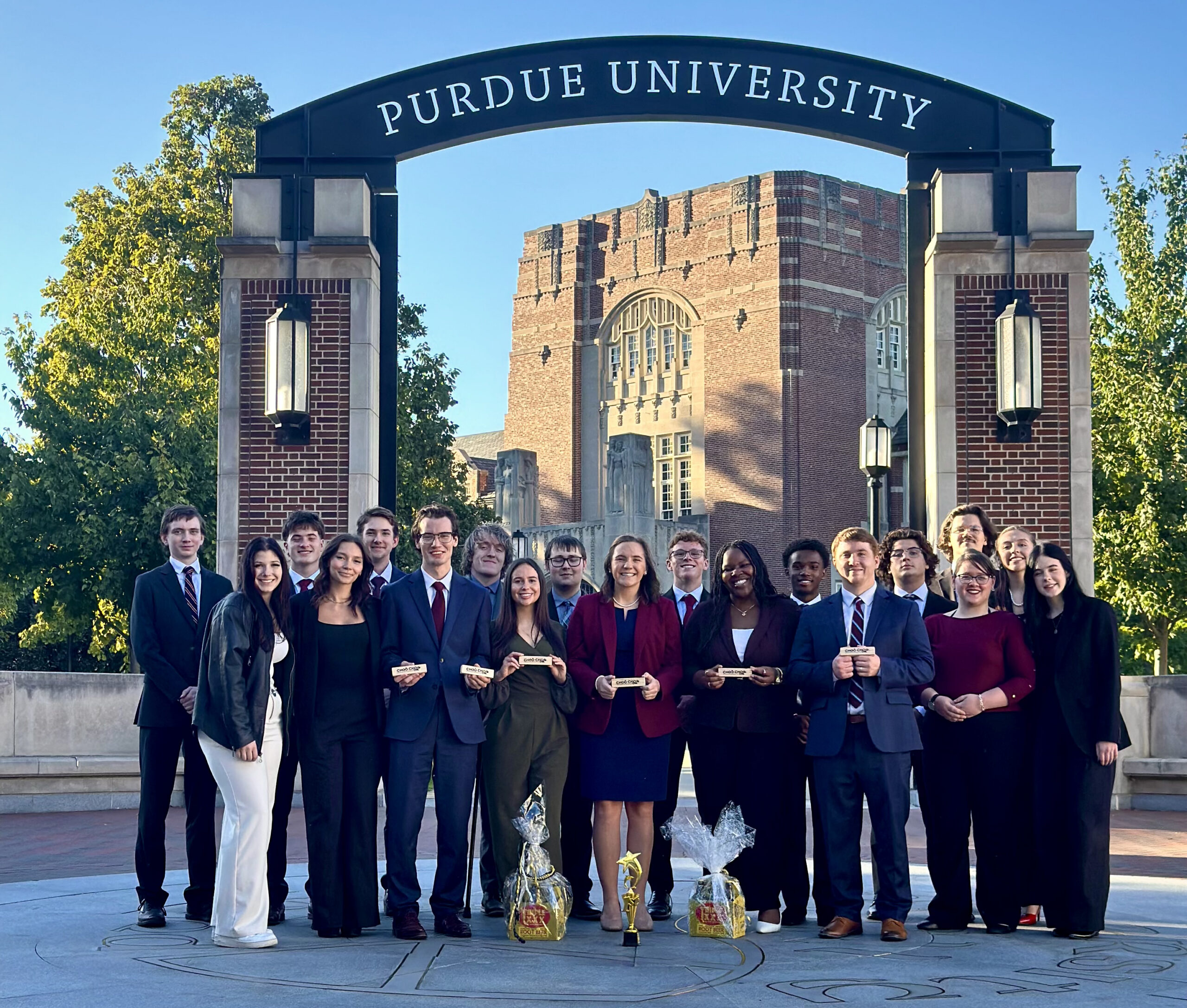 A group of students posing in business attire in front of the Purdue University gateway.