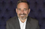 A middle-aged man with a beard, wearing a white shirt and dark blazer, smiling at the camera.