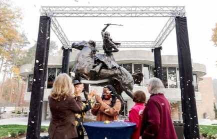 People applaud at the unveiling of a bronze statue of a woman riding a horse, a new landmark on the Northwood University campus.