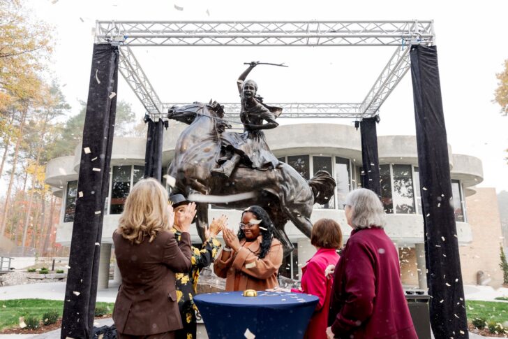 People applaud at the unveiling of a bronze statue of a woman riding a horse, a new landmark on the Northwood University campus.