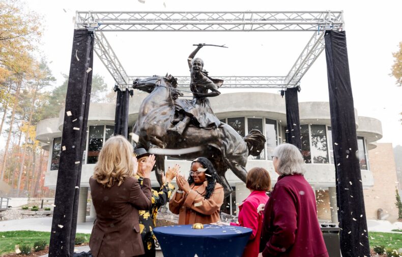 People applaud at the unveiling of a bronze statue of a woman riding a horse, a new landmark on the Northwood University campus.