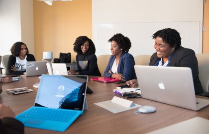 Four people are engaged in a meeting around a conference table with laptops open.