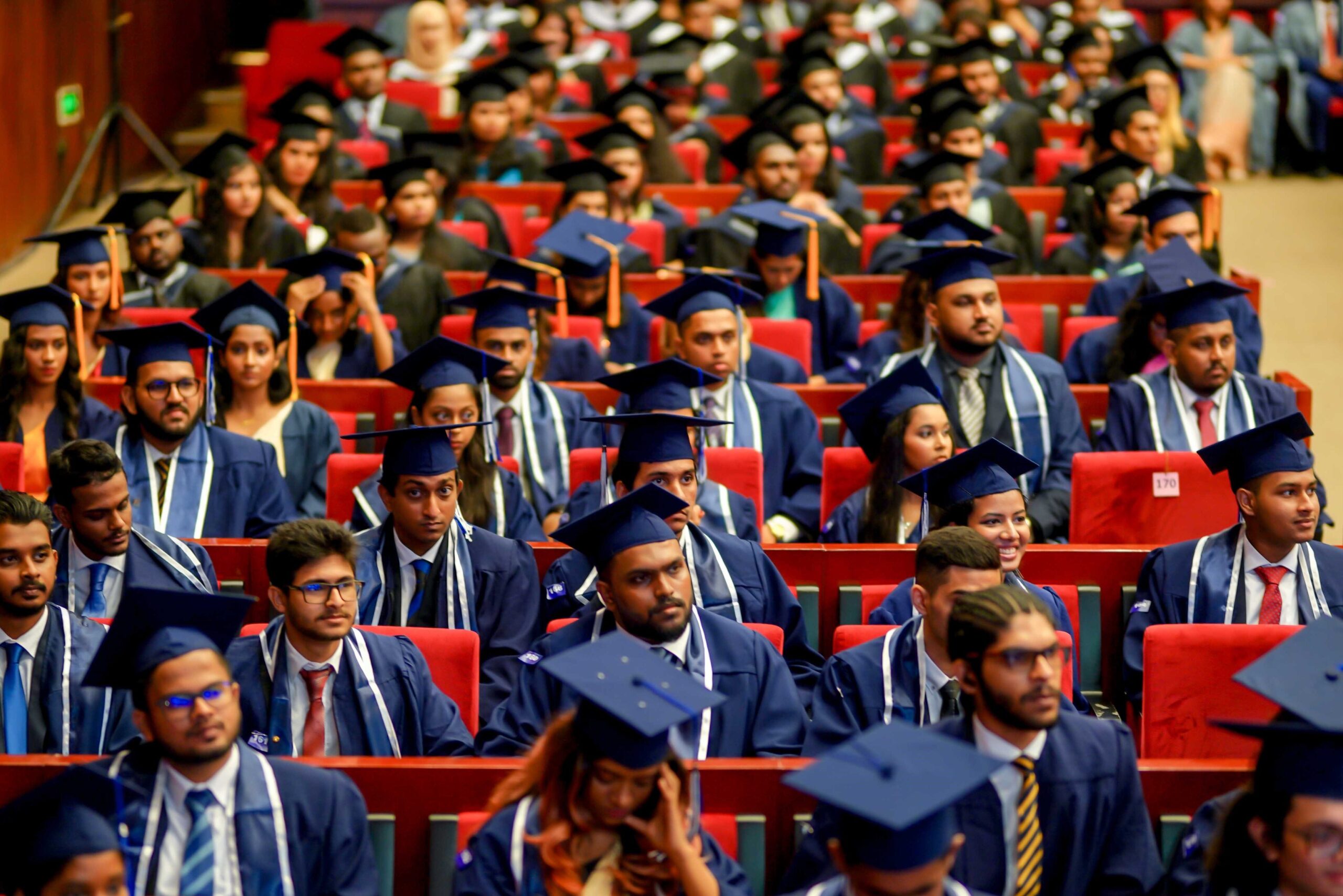 A large group of graduates in caps and gowns from Northwood University's International Admissions program sit in rows of red chairs during the ceremony.