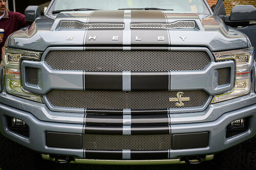 Close-up of the front grille of a grey Shelby truck with black and white stripes, displaying the Shelby name and logo.